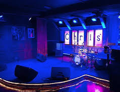 Stage with musical instruments and illuminated letters spelling 'Chris' in a dimly lit venue.