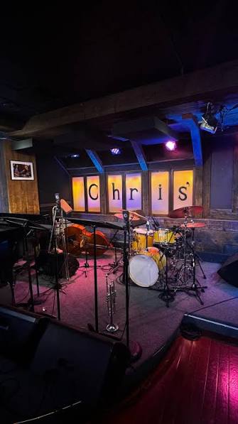 Empty stage with musical instruments and microphones, illuminated by colorful stage lights, in a dimly lit venue.