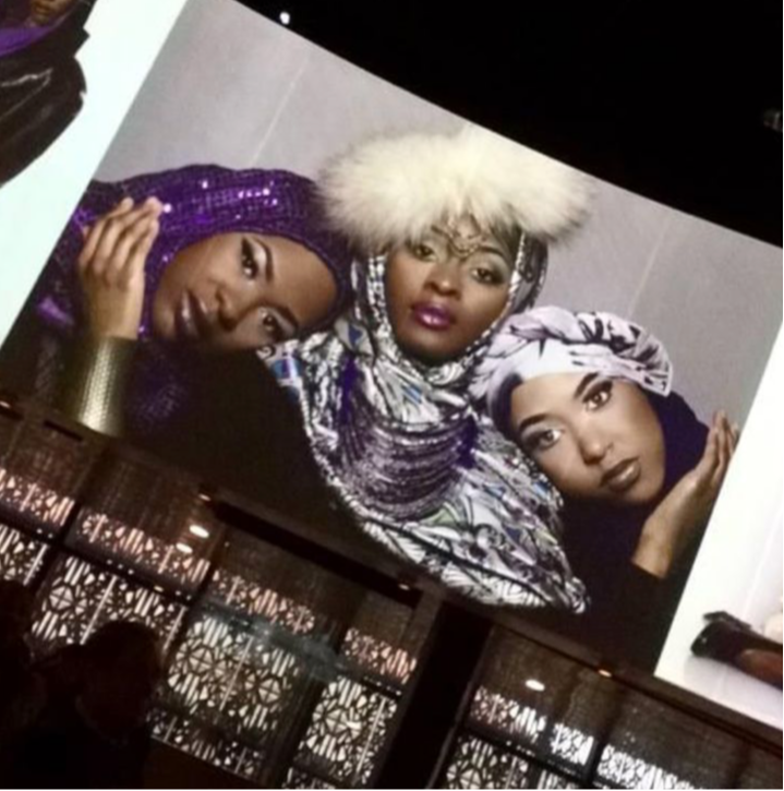 Three women wearing headscarves and accessories pose closely together, with a plain background. The image appears upright.