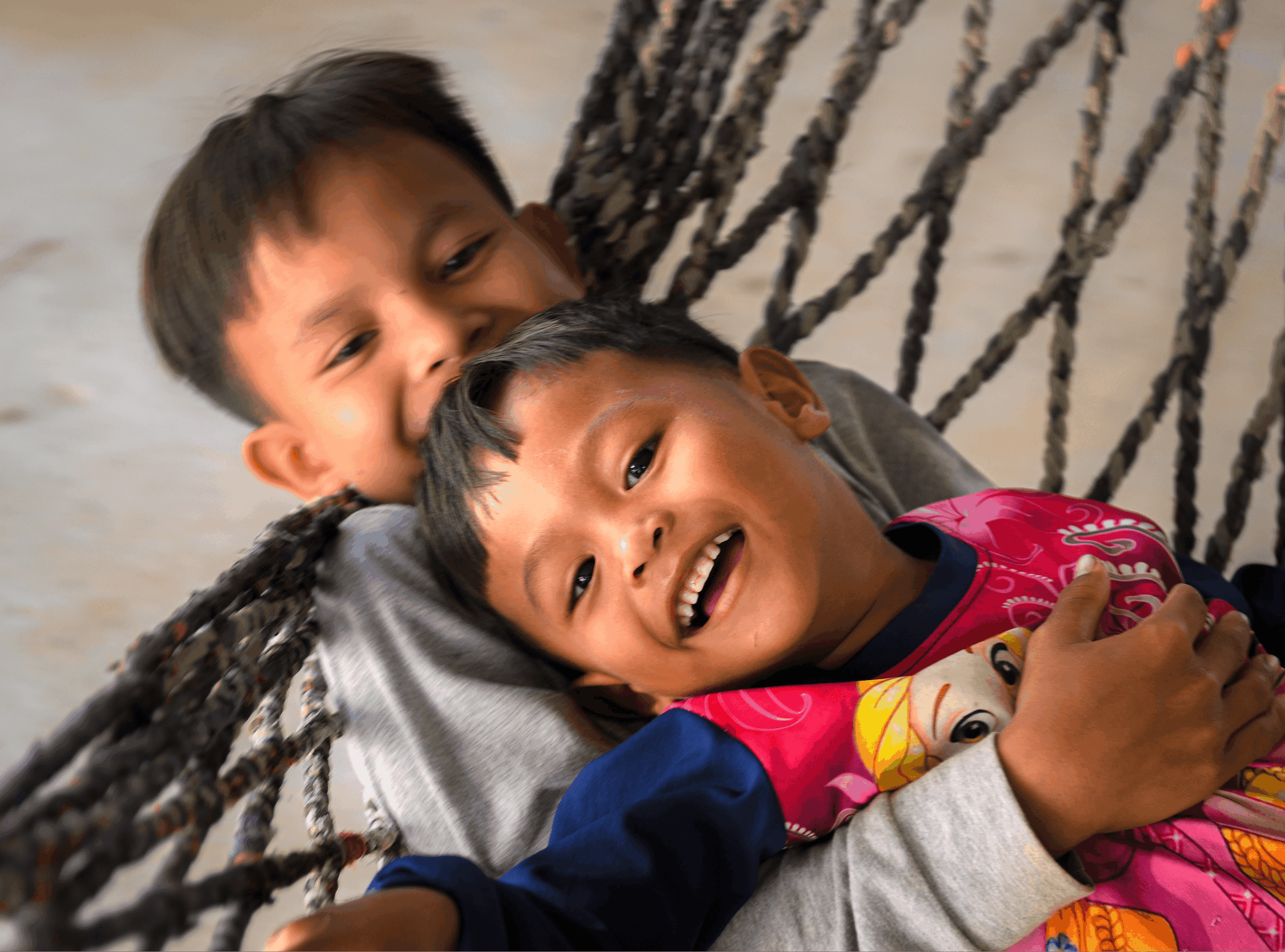 Two children lying on a hammock, smiling and playing together.
