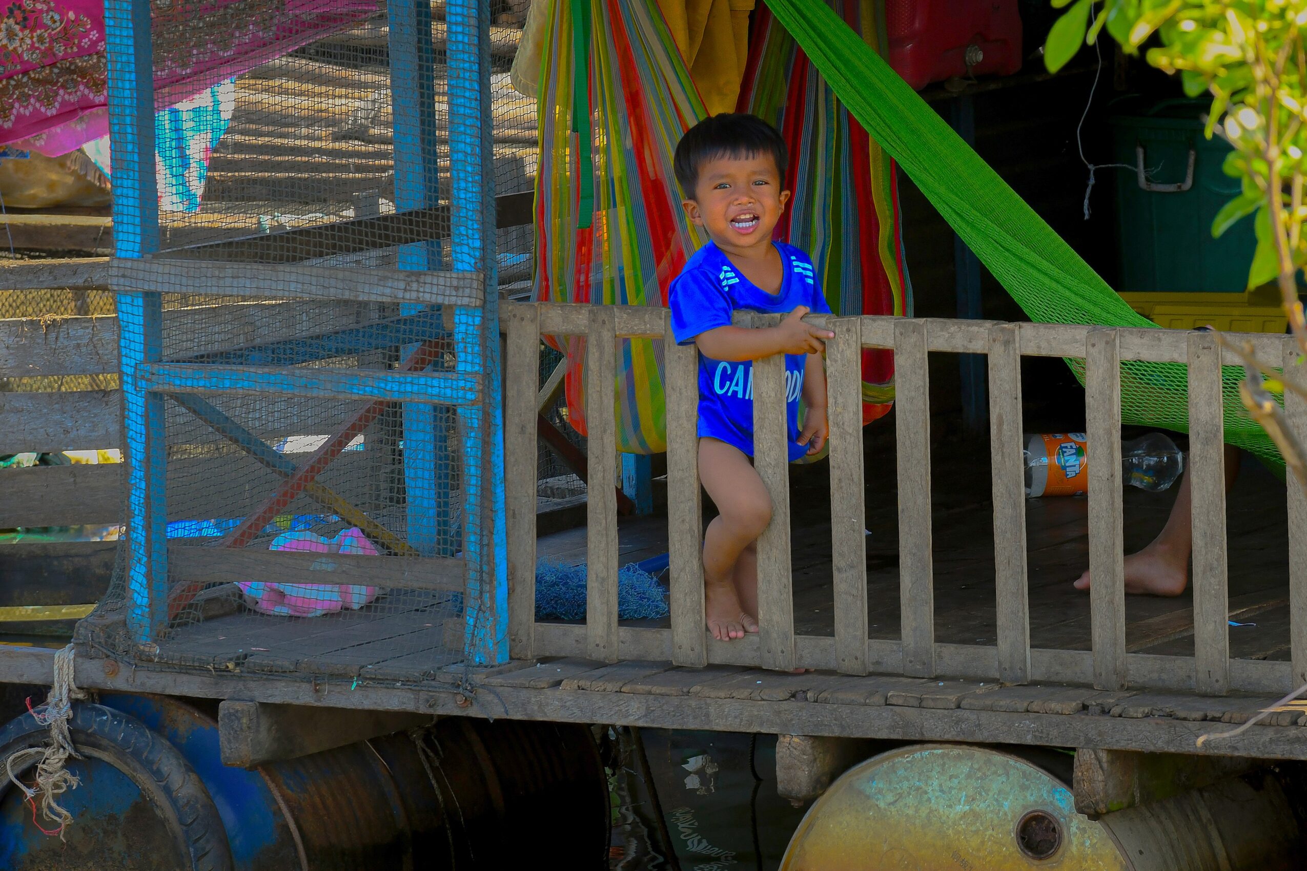Child standing on a wooden platform, smiling, with colorful decorations in the background.