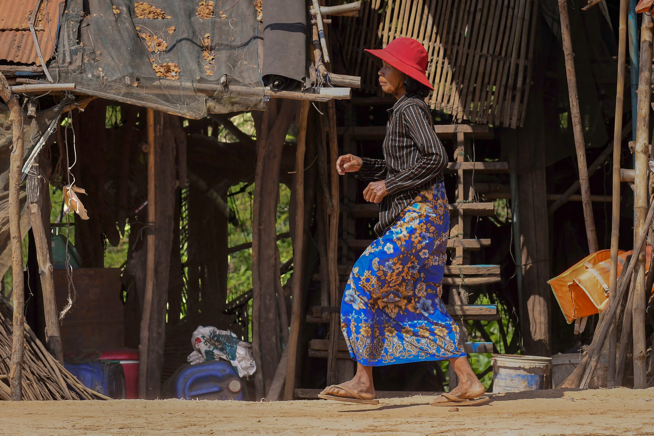 Woman wearing a red hat and patterned skirt walking on wooden stairs in a rustic setting