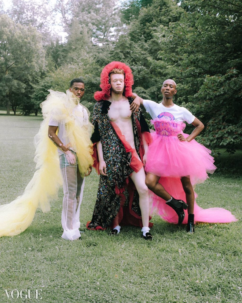 Three people in colorful, elaborate costumes standing outdoors on grass with trees in background.