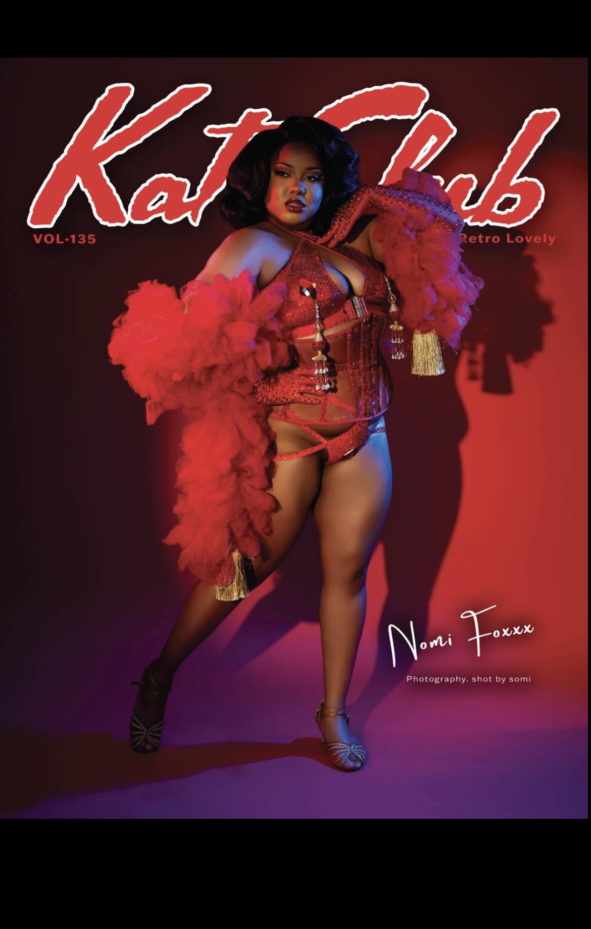 Woman in red outfit holding a large pink feathered accessory, magazine cover with red and black background.