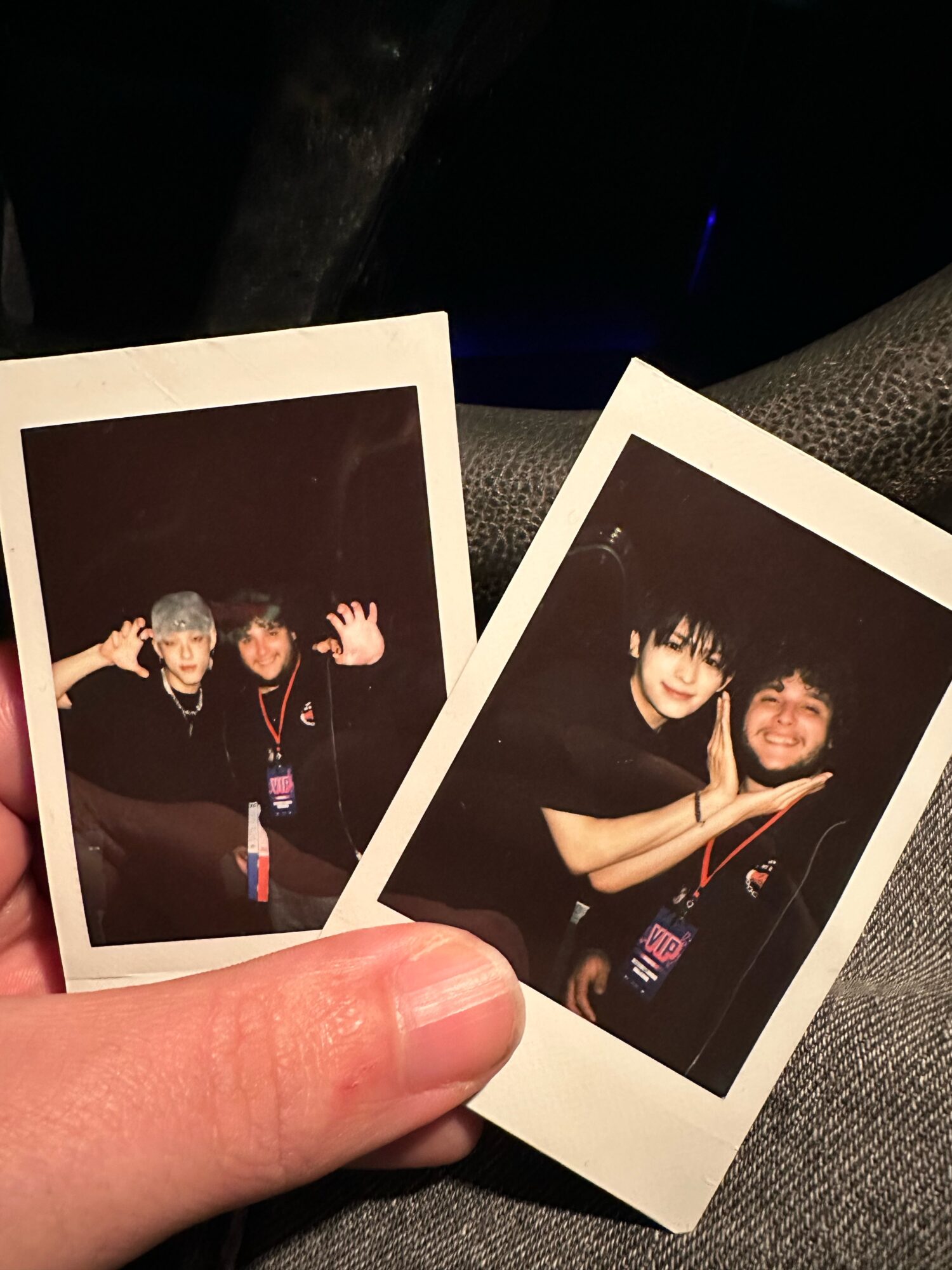 Two Polaroid photos held by a person's hand, showing two people smiling and posing together, dark background, casual clothing.