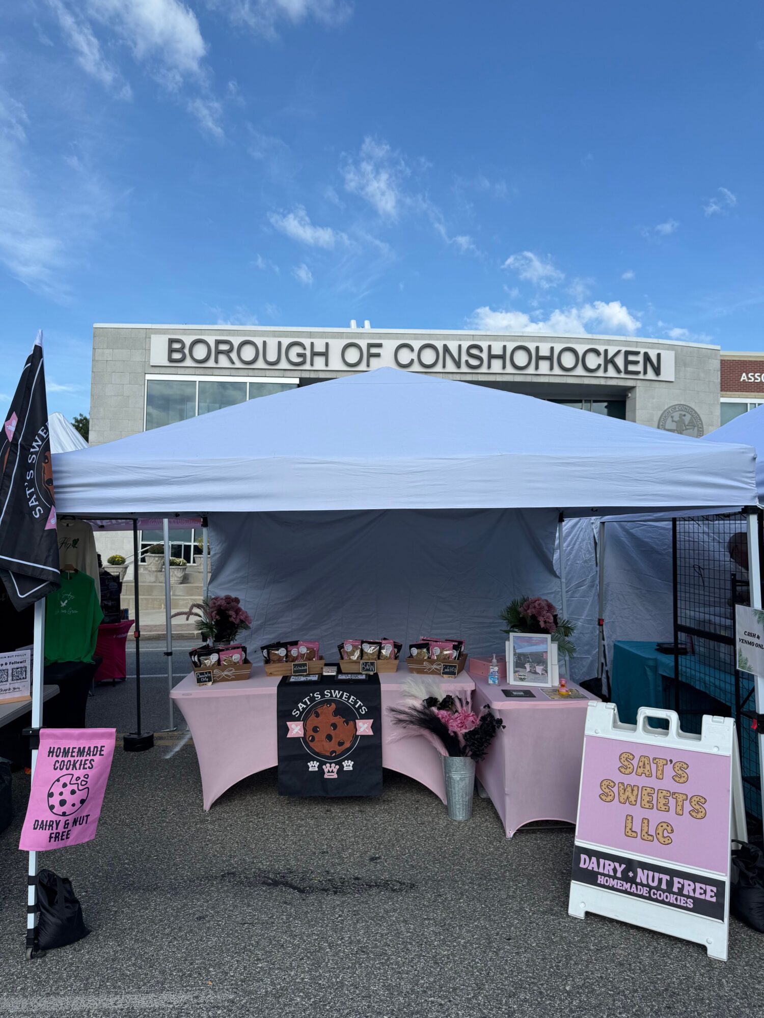 Outdoor booth with pink chairs and tables under a white tent, sign reading 'Borough of Conshohocken,' and pink signs on tables.