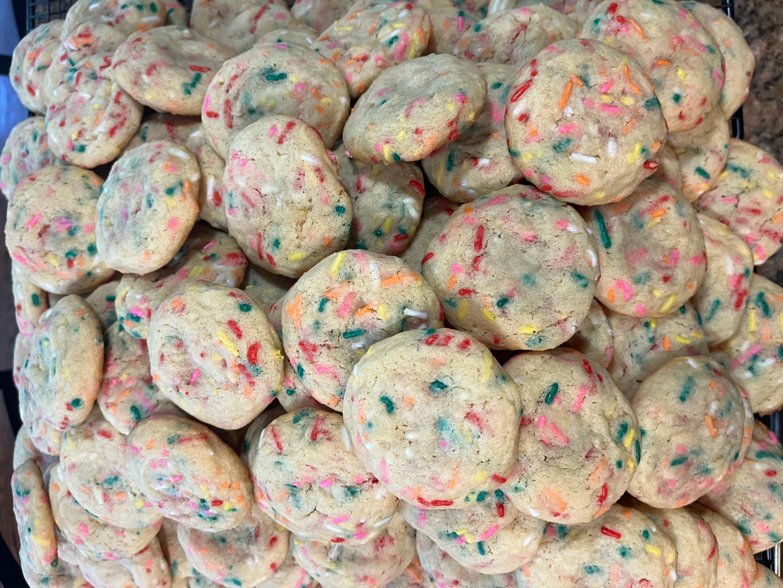 Colorful sprinkled cookies piled together, with a variety of bright colors on a light background.