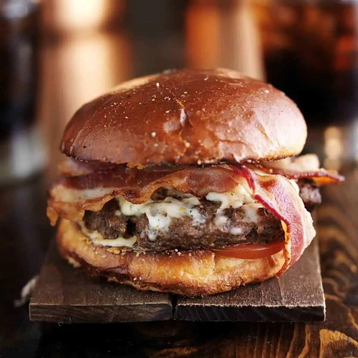 A burger with a bun, bacon, cheese, a beef patty, tomato, and lettuce on a wooden surface.