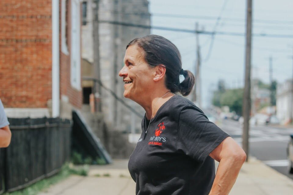 Smiling woman with dark hair tied back, wearing a black shirt, standing outdoors on a city street.