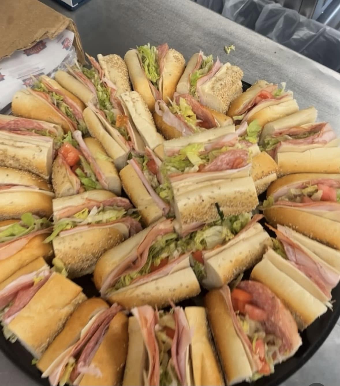 Tray of assorted sandwiches with bread, lettuce, tomato, and meats arranged in a circular pattern.