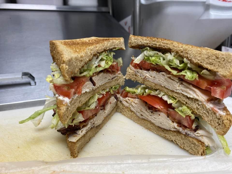 Two halves of a sandwich with lettuce, tomato, and turkey on toasted bread, placed on a white surface.