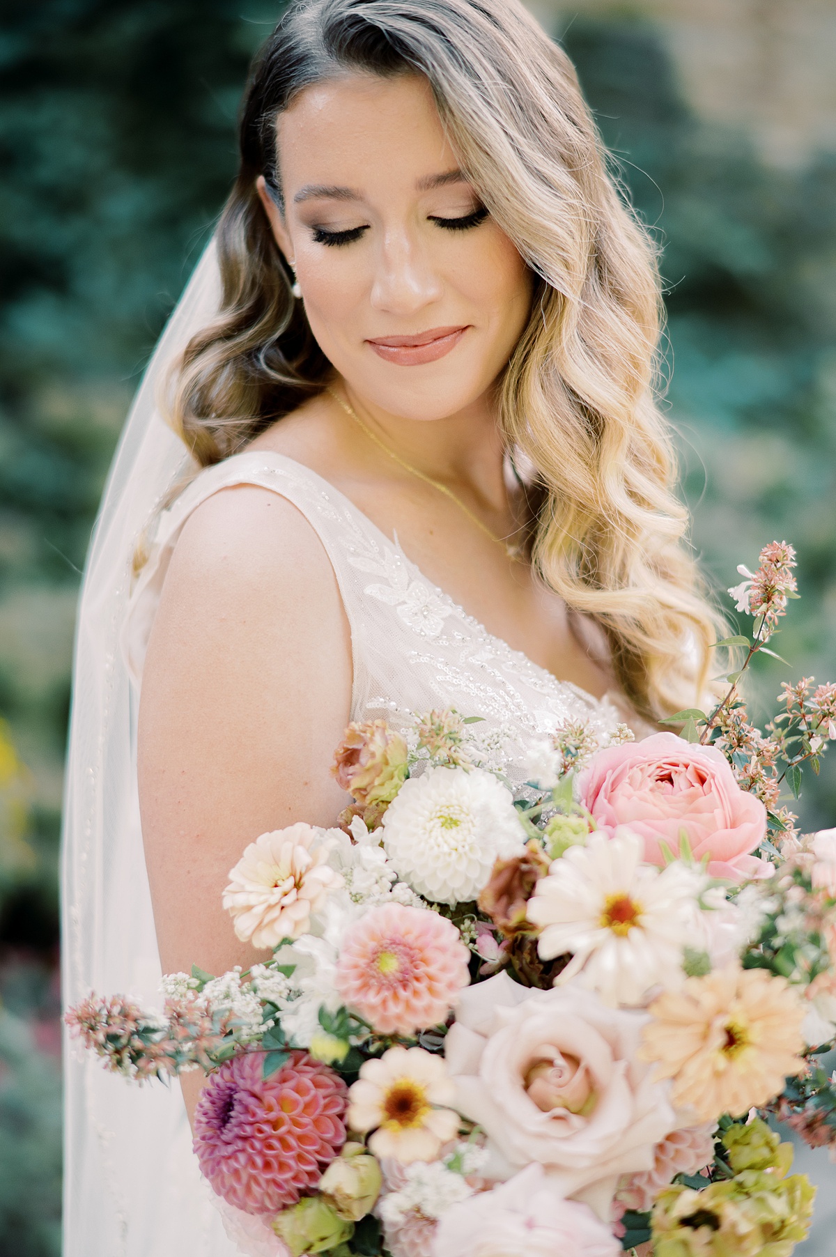A woman in a wedding dress holding a bouquet of flowers, smiling with eyes closed outdoors.